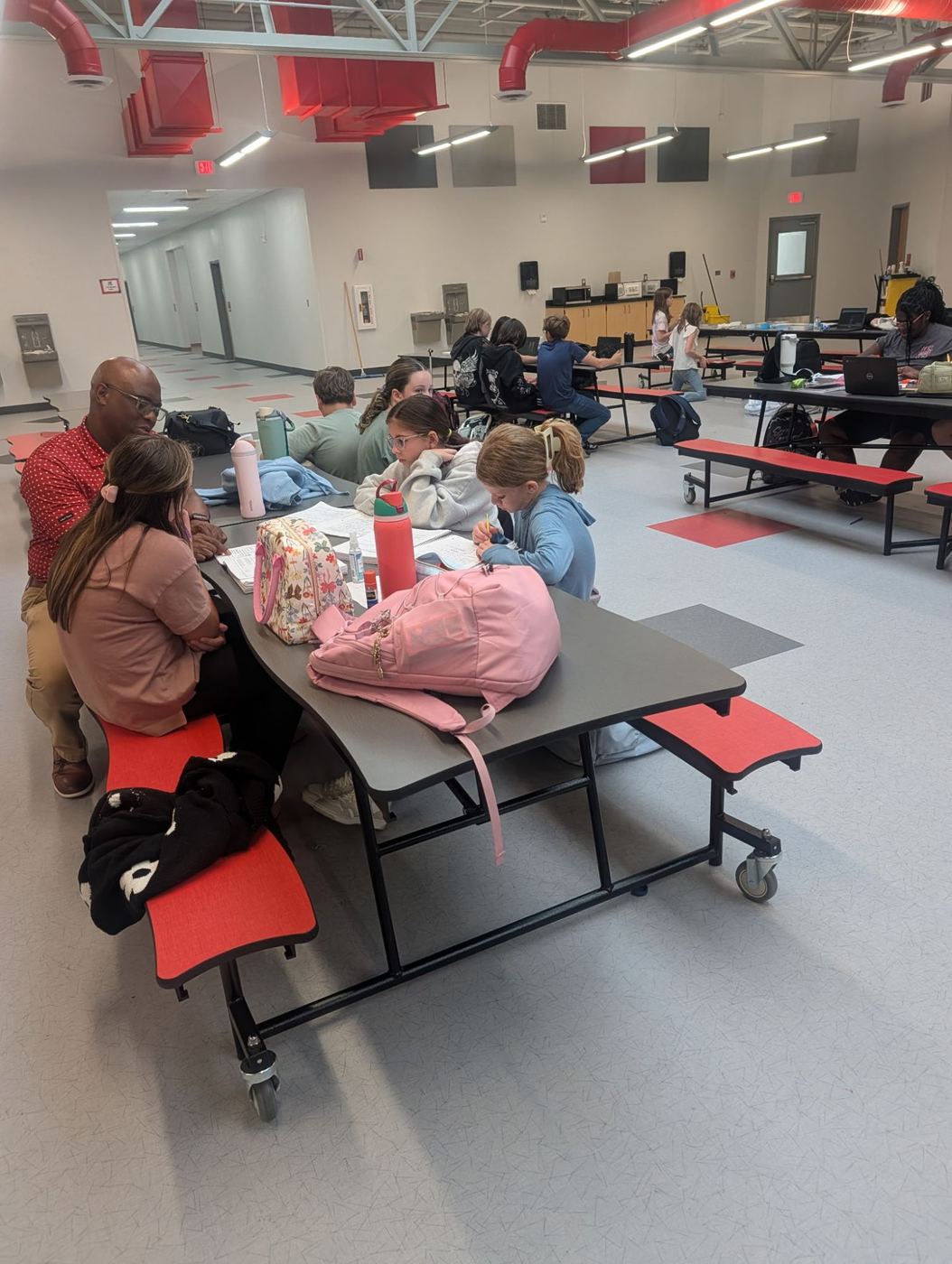 A staff member helping students with homework at a cafeteria table