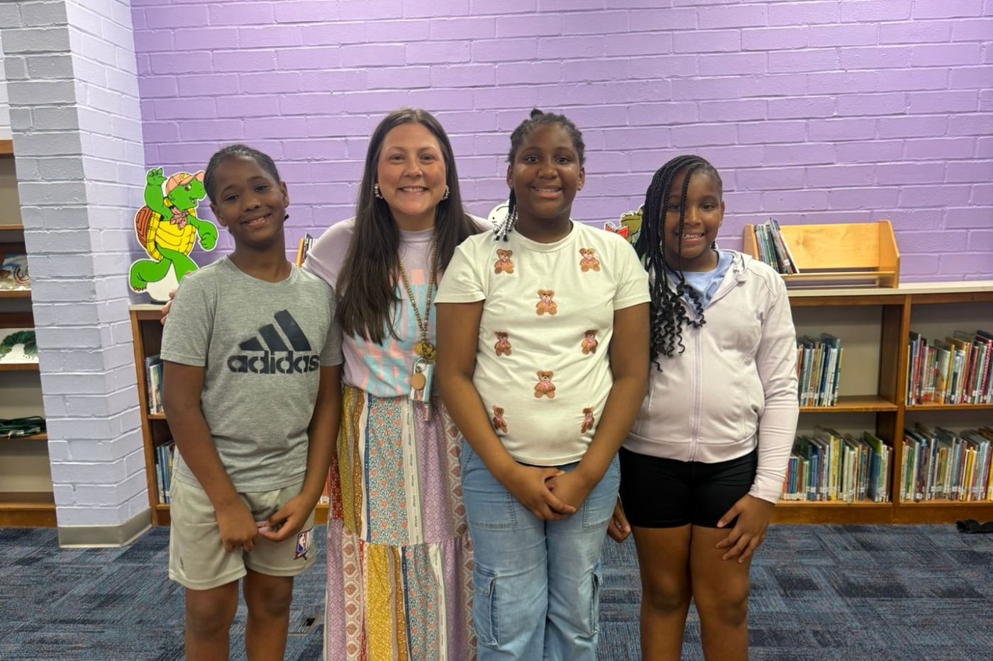 A staff member standing with three smiling students in a school library