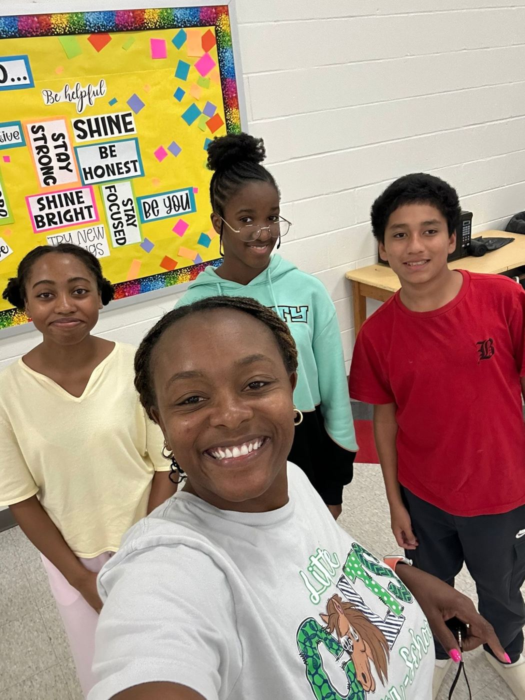 A Little Colts staff member in a Little Colts shirt taking a selfie with three middle schoolers