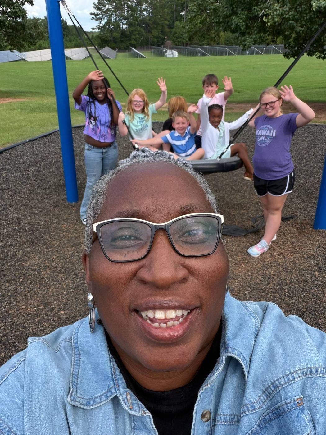 Kids waving from the playground swing with a staff member smiling in front