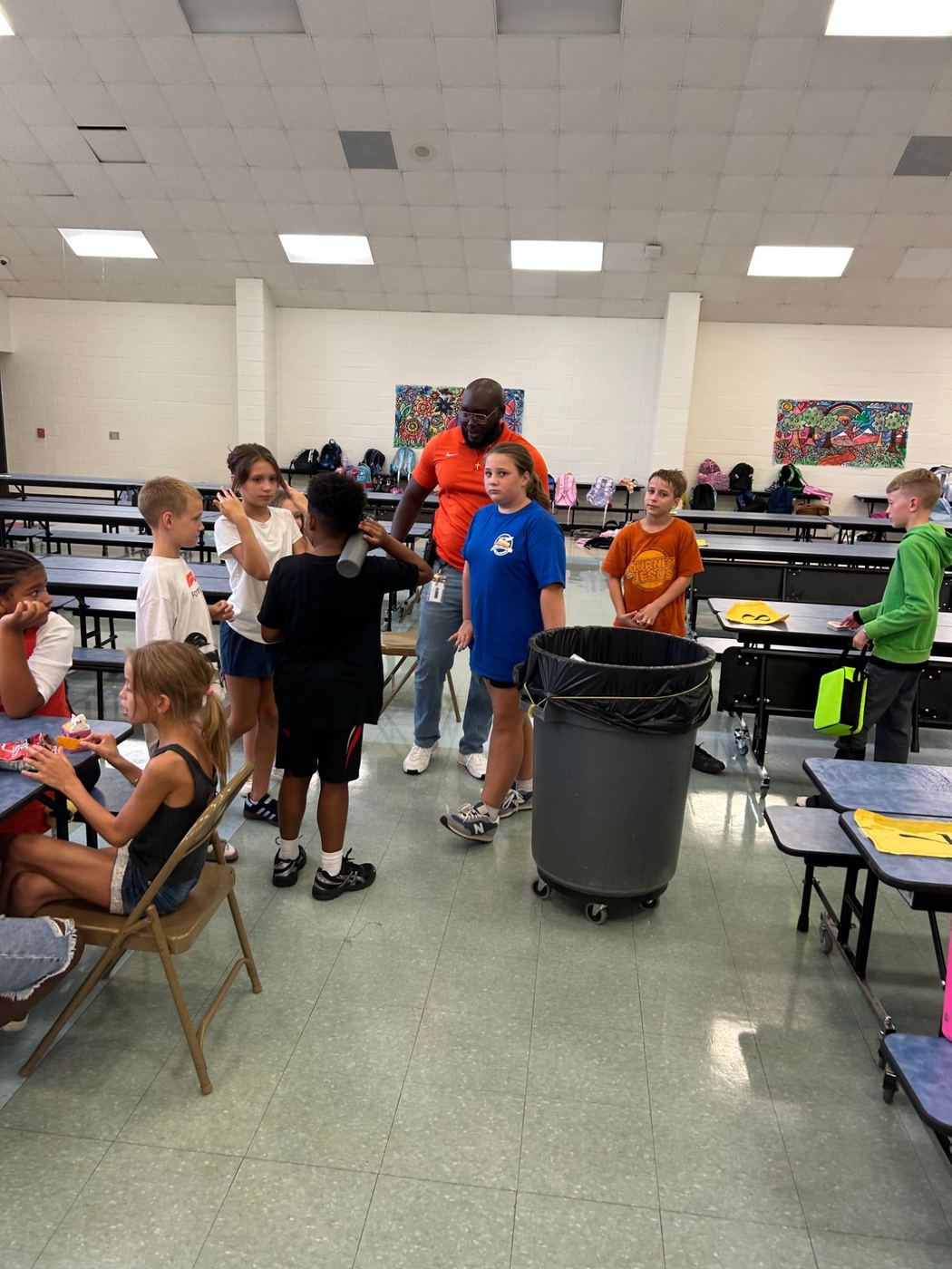 Kids having an afternoon snack and chatting with a staff member in the cafeteria