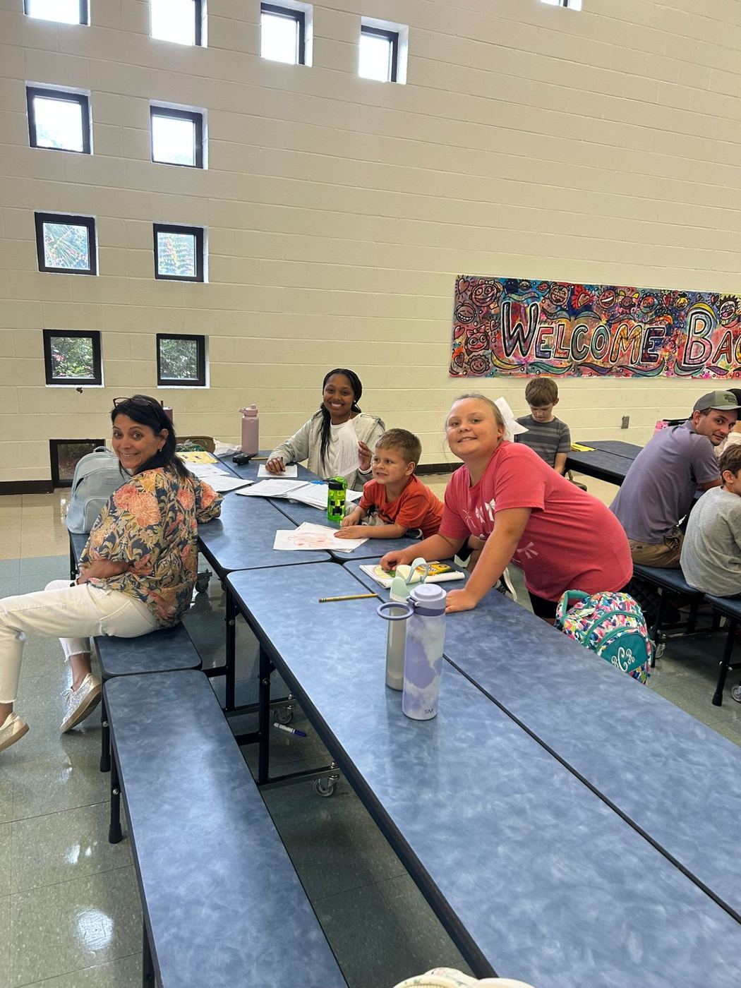 Staff and kids smiling at a table under a Welcome Back banner